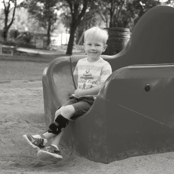 A boy sitting at the edge of an outdoor slide wearing a WalkOn junior AFO